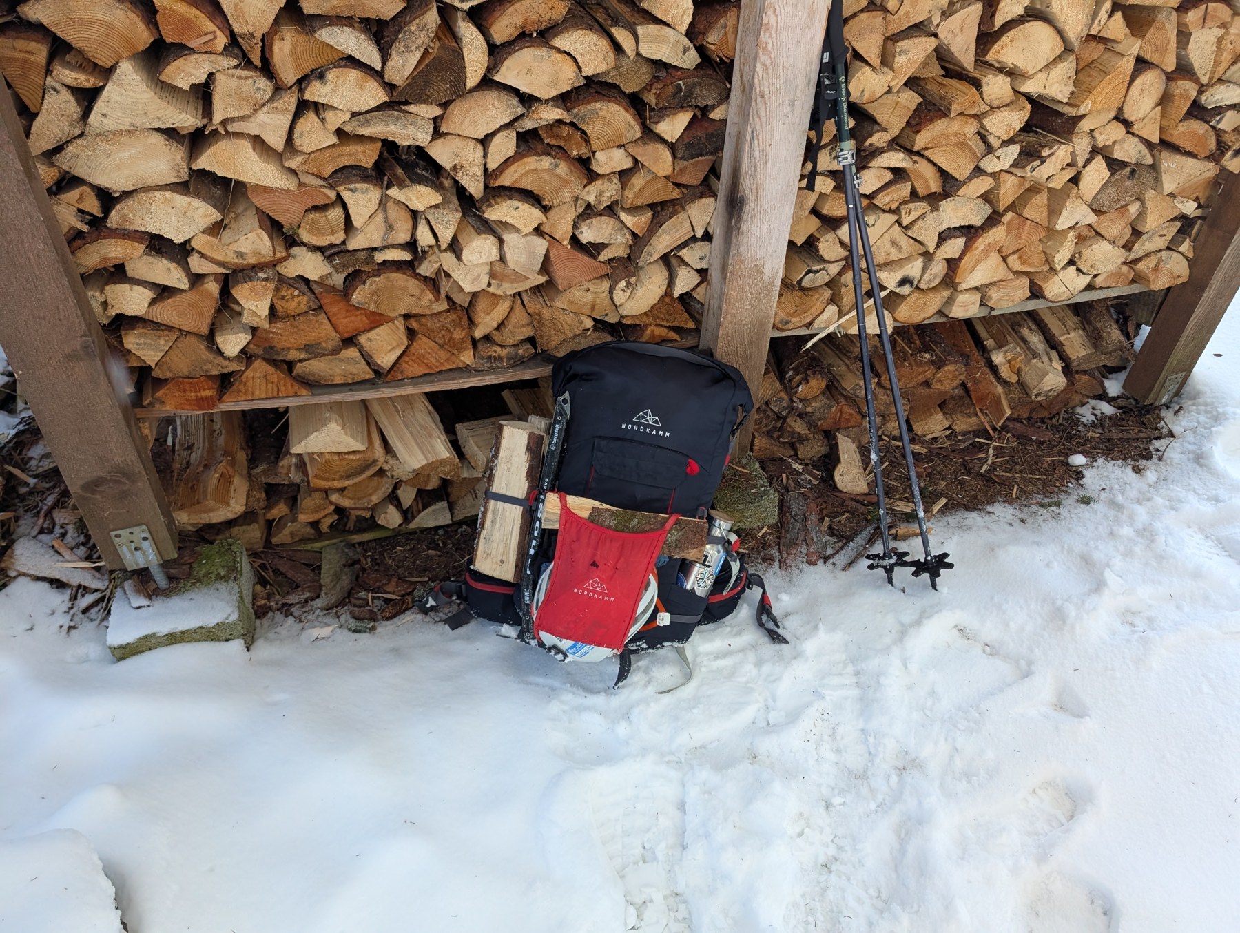 Brennholz, Rucksack und Skistöcke bei der Selbstversorgerhütte.
